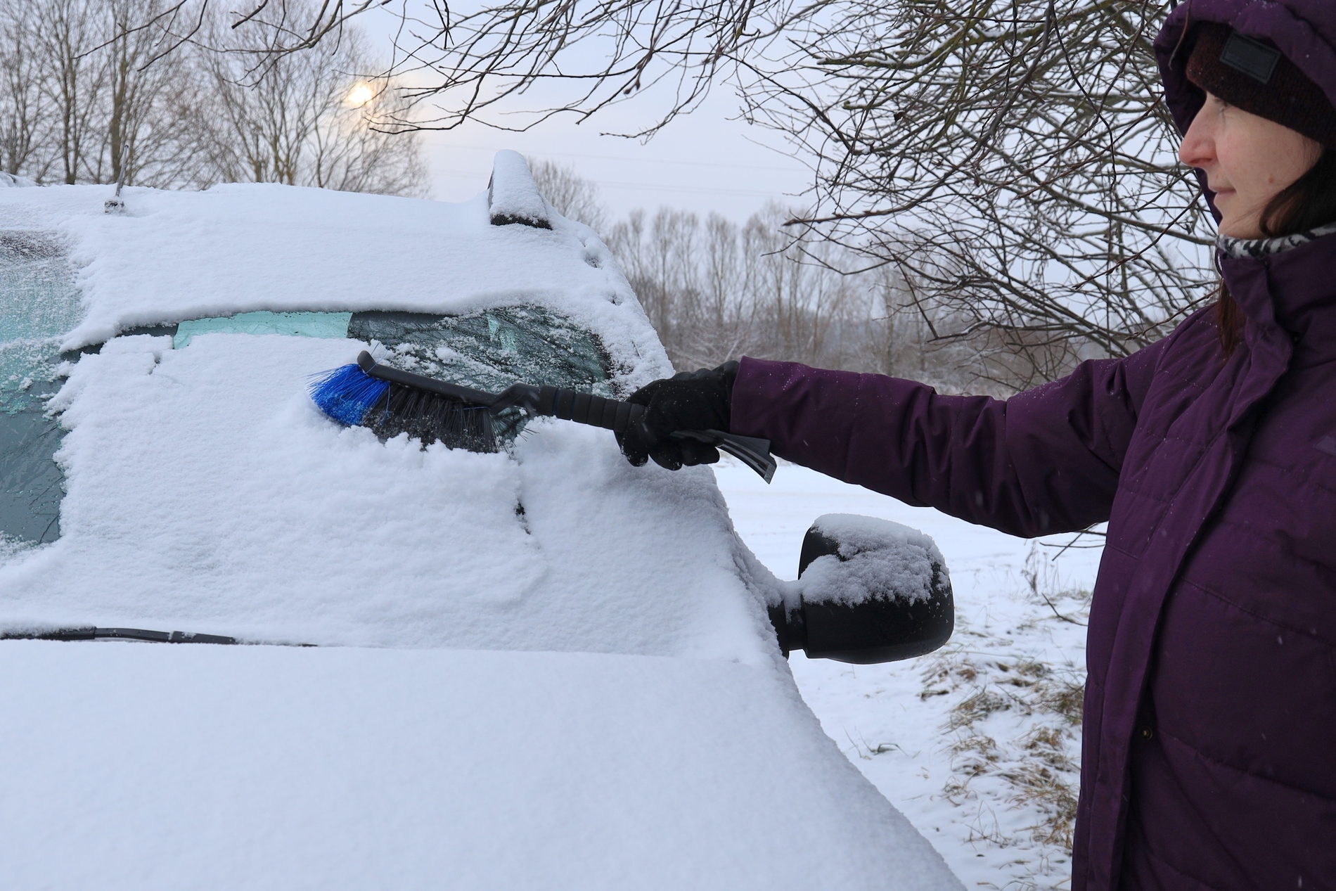 girl brushing snow off car windshield with soft brush